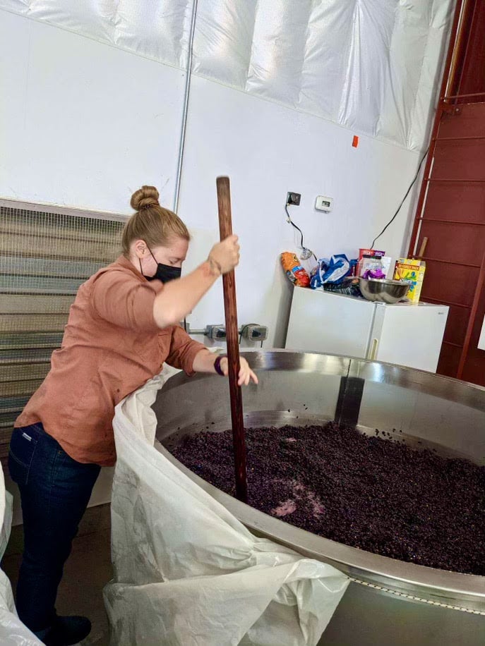 Intern does a punch down on a tank of Pinot Noir 