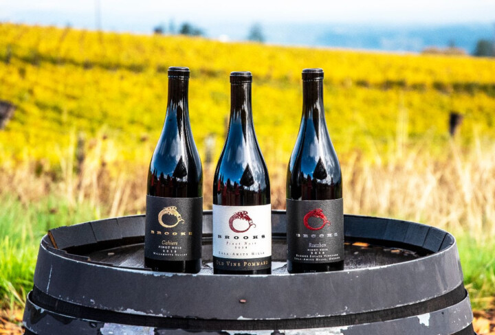 Three bottles of Pinot Noir clones on a wine barrel. 