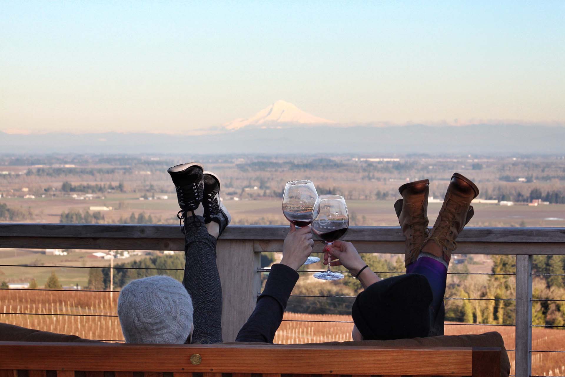 Two friends sitting on the Brooks patio, drinking wine and overlooking vineyards