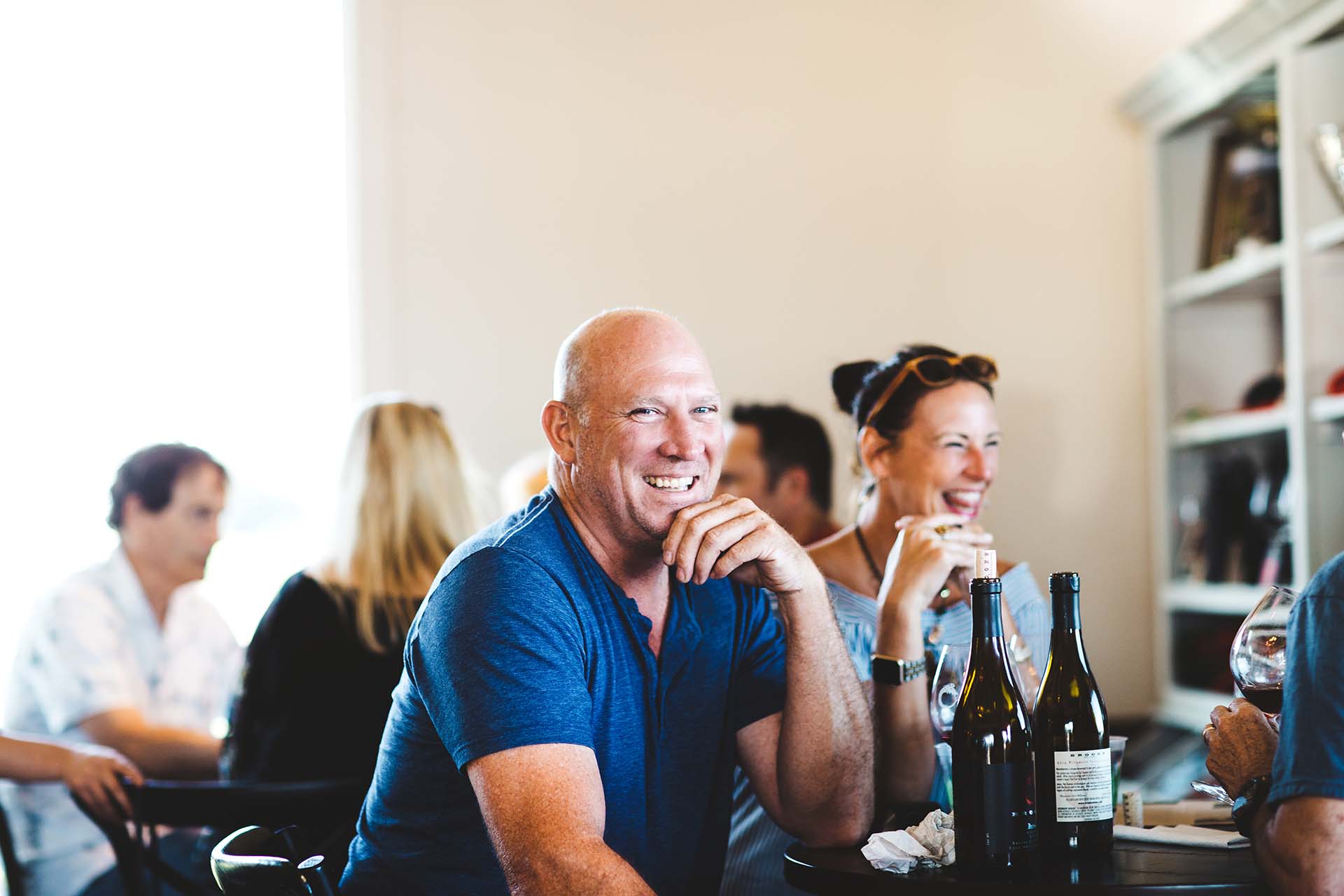 Smiling man looking at camera, with friends and wine at table