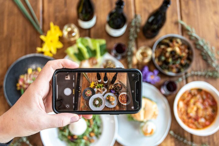 Person using photo to photograph Brooks Wine with a table covered in food
