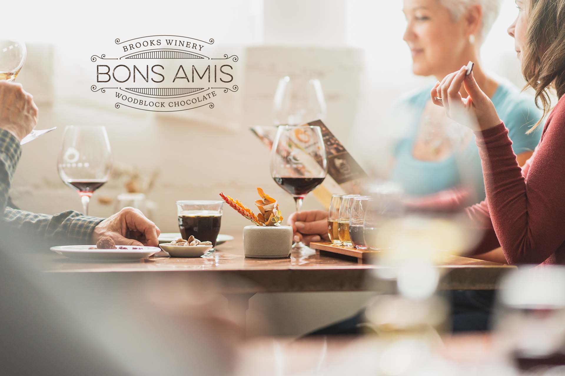 Friends sitting at table drinking Brooks wine and eating chocolate, with Brooks Bons Amis logo