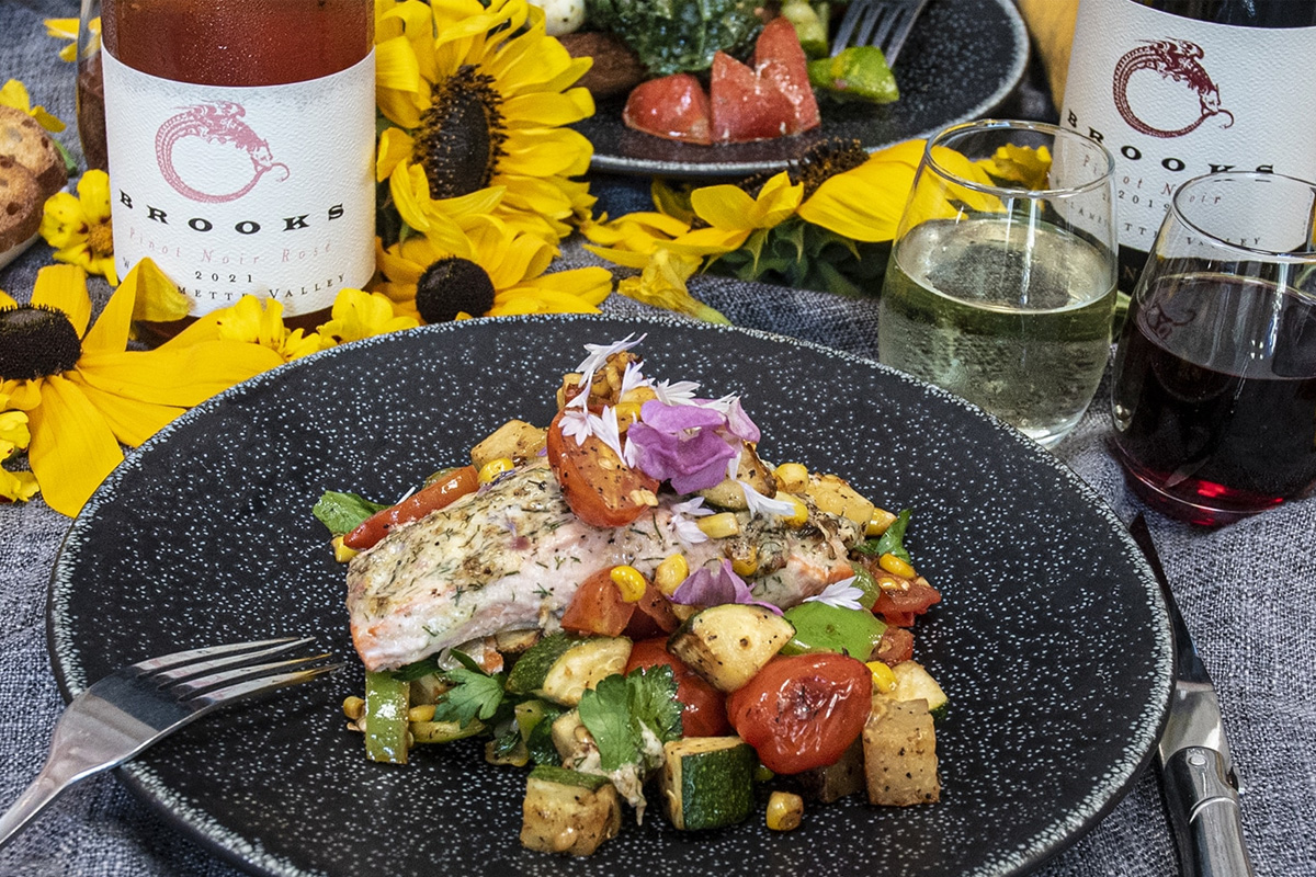 Dish of Salmon with Vegetables, one bottle of Brooks Rose, one bottle of Brooks Pinot Noir, and two stemless glasses.