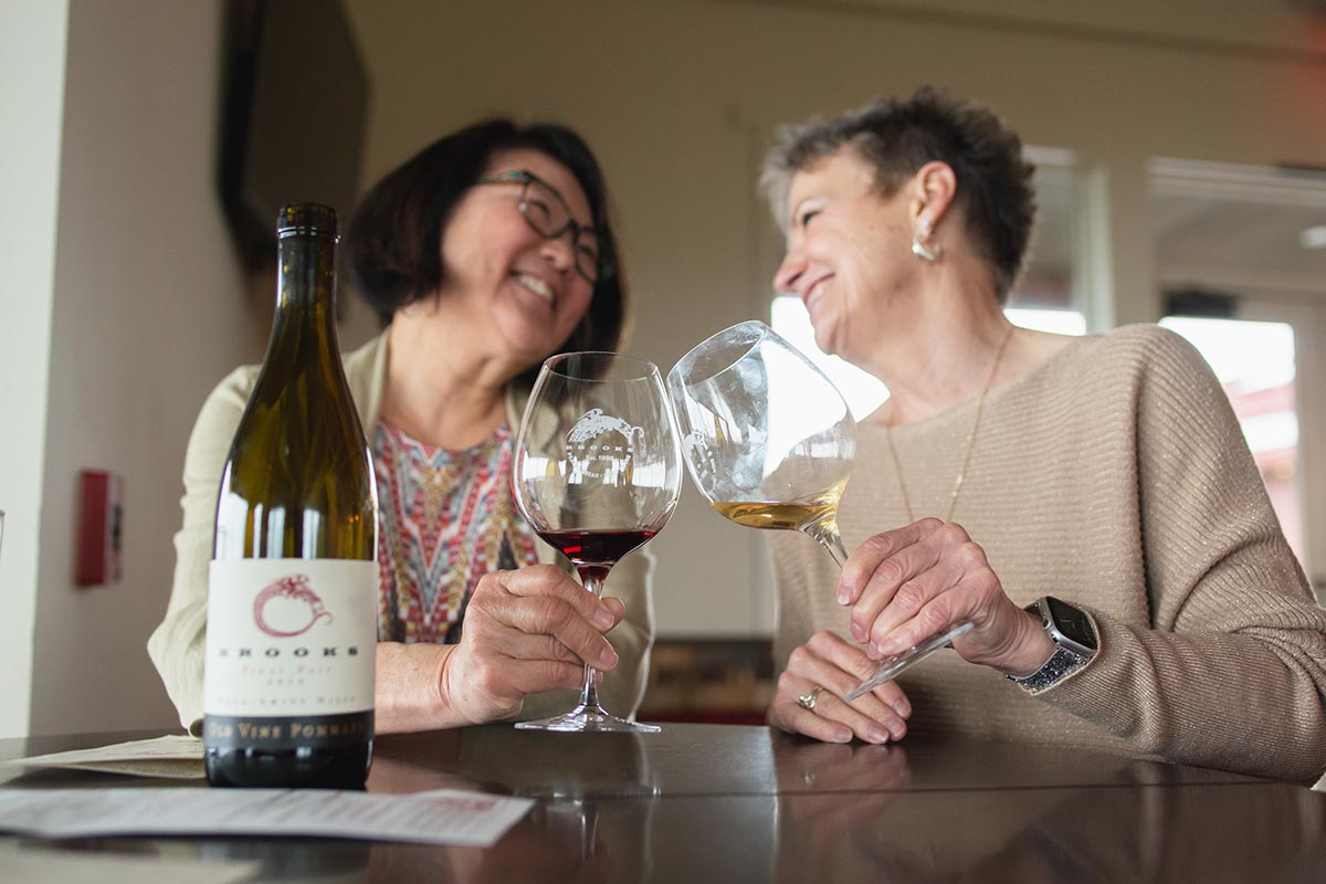 Two women smiling and toasting their glasses together while wine tasting. 