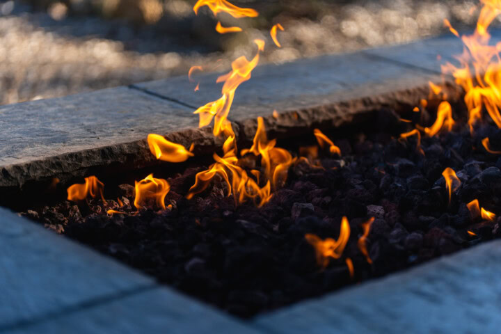 A close up of the flames within a fire pit surrounded by flagstone provides heat to outdoor seating.