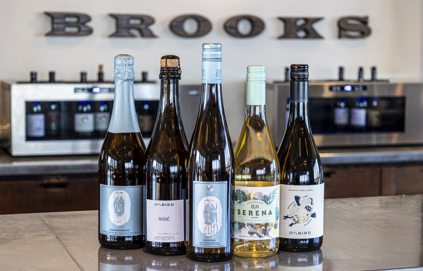 Five bottles of non-alcoholic wine sit atop a metal bar in front of the Brooks Wine logo in Amity, Oregon.