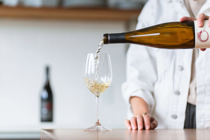 A woman in a white jacket observes wine etiquette by pouring a 5-ounce glass of white wine chilled to 50 degrees. 