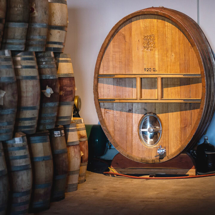 A oval, 920-gallon oak cask barrel  is prominently displayed next to stacked French oak barrel used to age bold red wines and oak-aged white wine. 