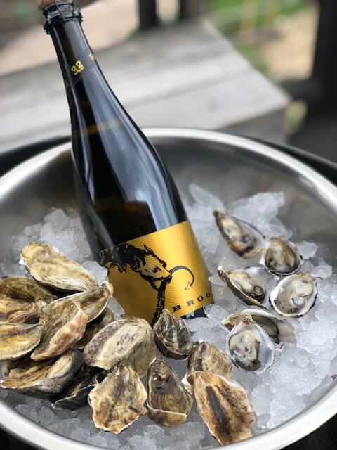 A metal bucket of ice chilling a crisp white wine to be paired with freshly shucked oysters. 