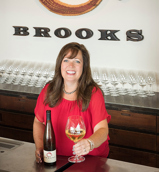 Director of Wine Club Happiness, Heather, stands with a glass of Brooks Riesling behind the bar.